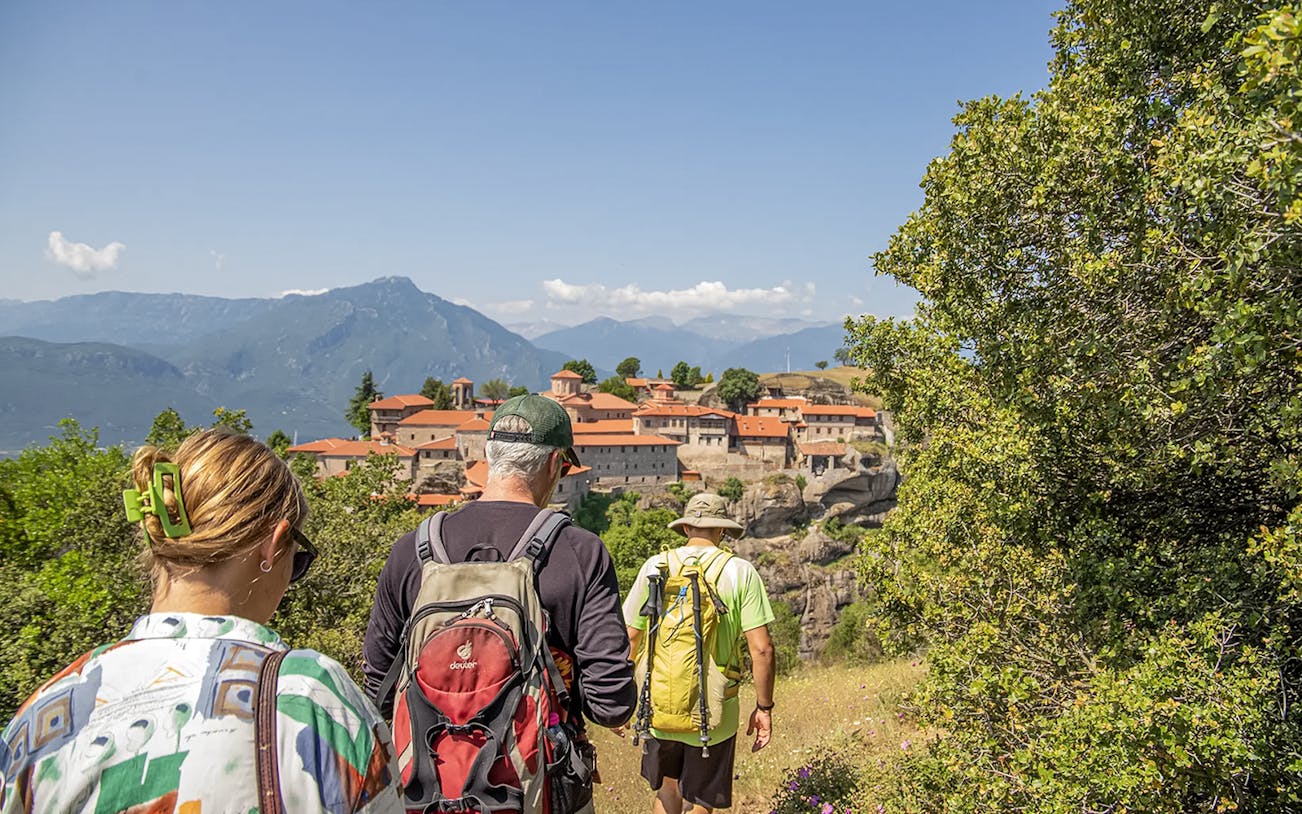 Guests hiking towards Meteora monastery with mountain backdrop.