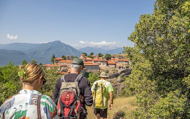 Guests hiking towards Meteora monastery with mountain backdrop.