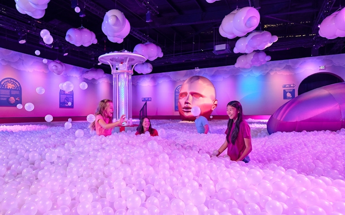 Visitors enjoying a ball pit at Bubble Planet Atlanta with colorful lighting and decor.