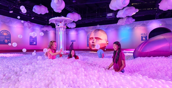 Visitors enjoying a ball pit at Bubble Planet Atlanta with colorful lighting and decor.