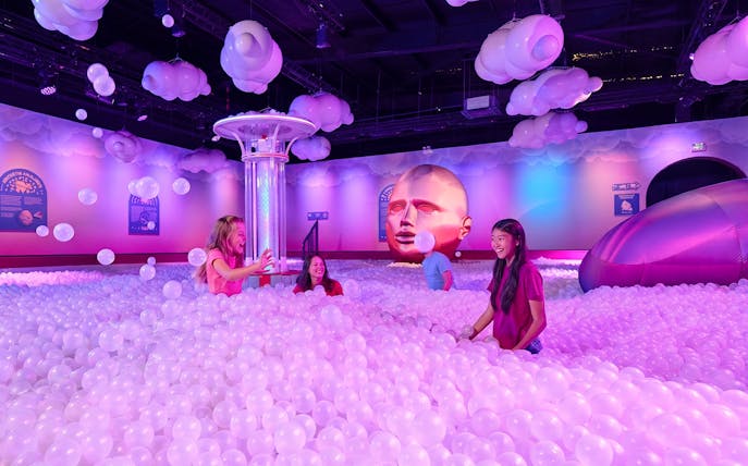 Visitors enjoying a ball pit at Bubble Planet Atlanta with colorful lighting and decor.