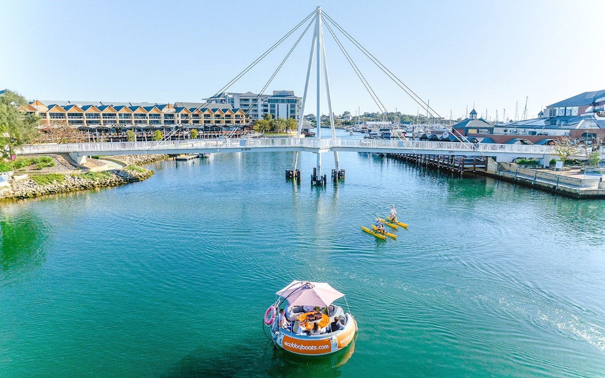 BBQ boat on Mandurah waters near bridge, with kayakers nearby.