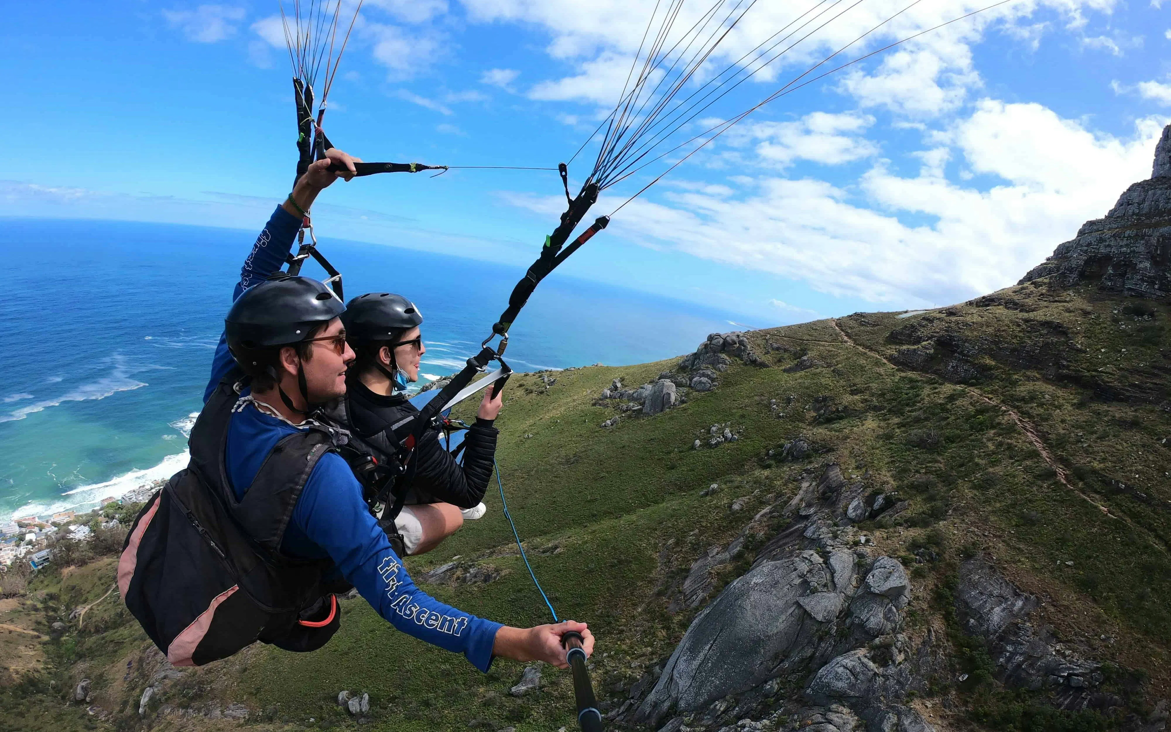 Tandem paragliders soaring over Cape Town coastline with mountain view.