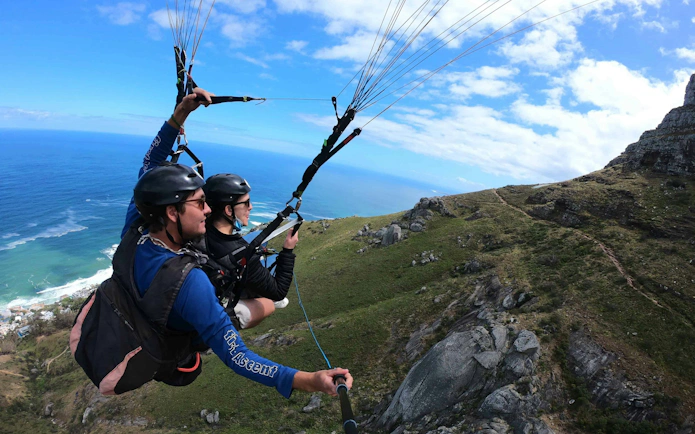 Tandem paragliders soaring over Cape Town coastline with mountain view.