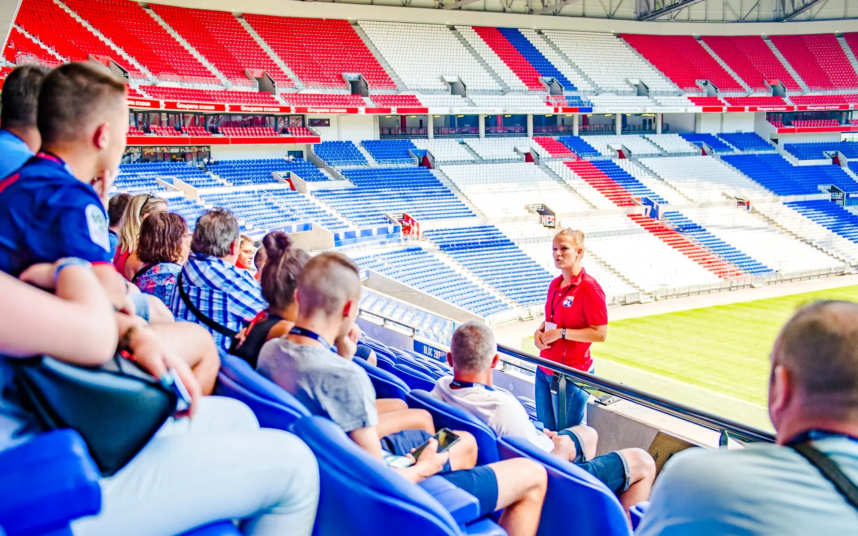 Tour group at Olympique Lyonnais stadium, Lyon, France, with guide explaining the venue.