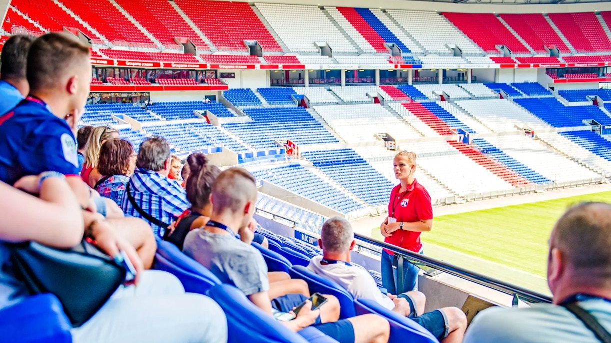 Tour group at Olympique Lyonnais stadium, Lyon, France, with guide explaining the venue.