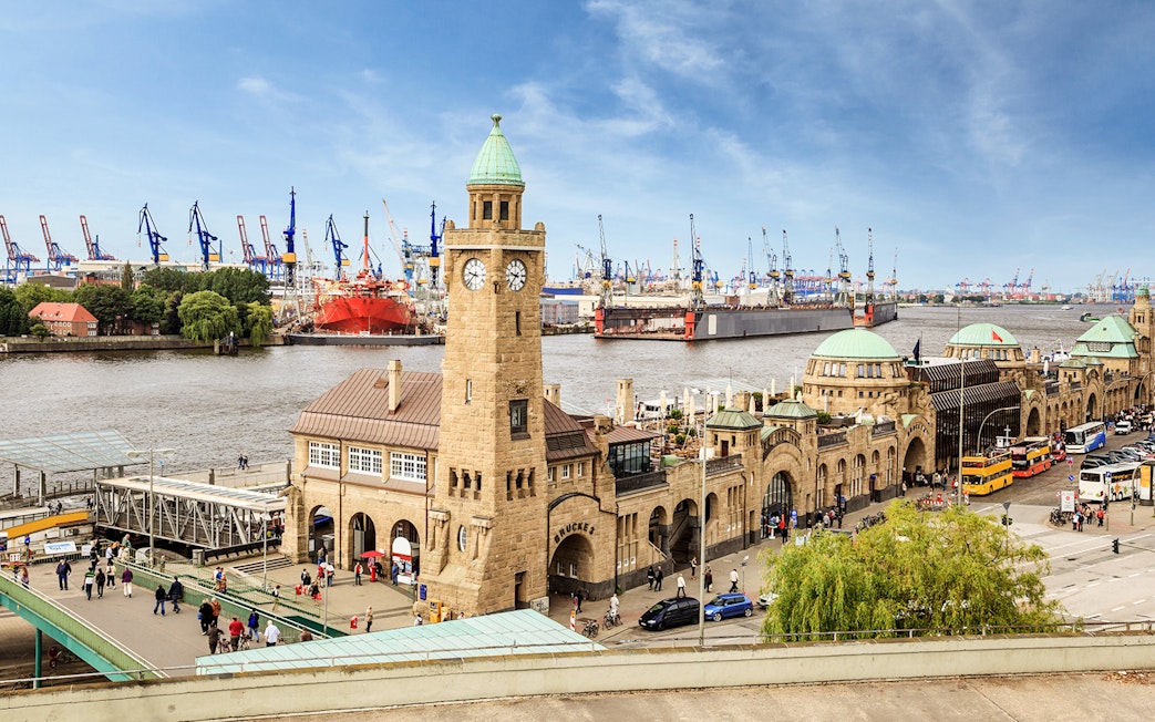Landungsbrücken pier and clock tower in Hamburg with harbor cranes in the background.