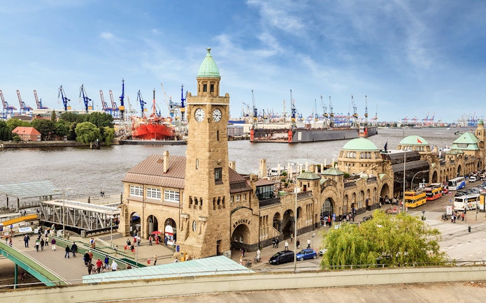 Landungsbrücken pier and clock tower in Hamburg with harbor cranes in the background.