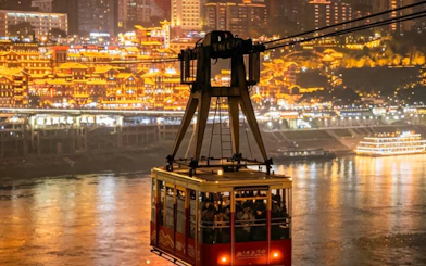 Cable car crossing river with illuminated cityscape in Chongqing at night.
