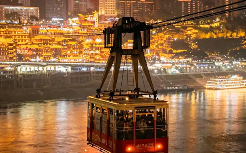 Cable car crossing river with illuminated cityscape in Chongqing at night.