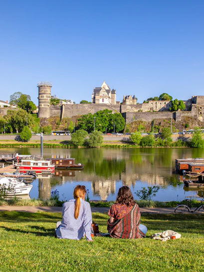 Two people sitting by the river with a view of Château d'Angers, Loire Valley.