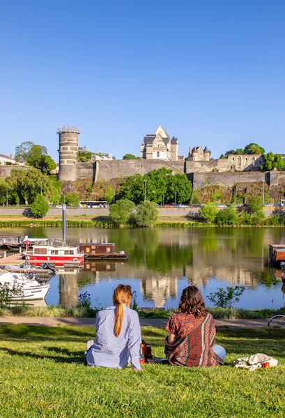 Two people sitting by the river with a view of Château d'Angers, Loire Valley.
