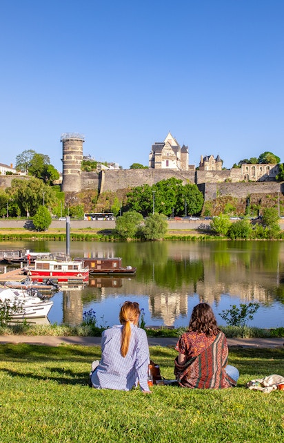 Two people sitting by the river with a view of Château d'Angers, Loire Valley.