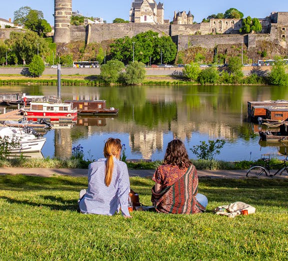 Two people sitting by the river with a view of Château d'Angers, Loire Valley.
