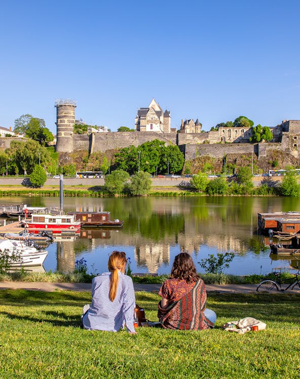 Two people sitting by the river with a view of Château d'Angers, Loire Valley.