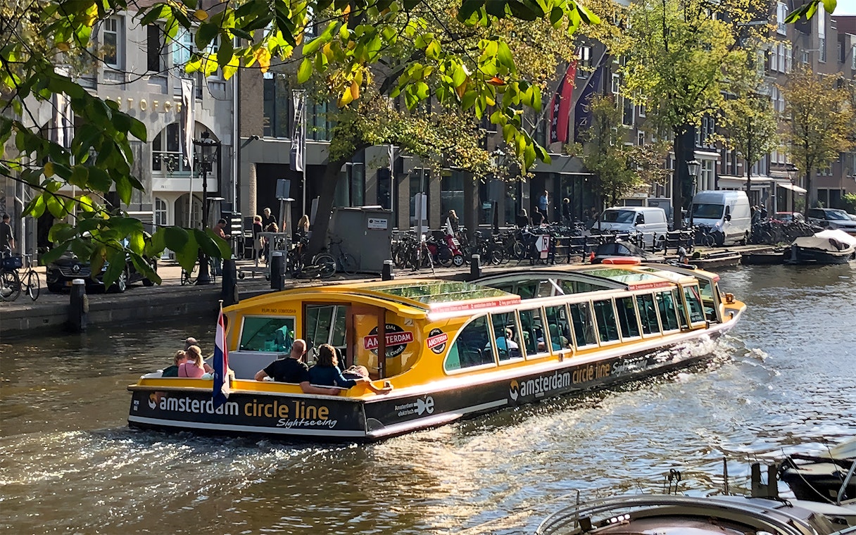 Canal cruise boat on Amsterdam canal with passengers and city buildings in the background.
