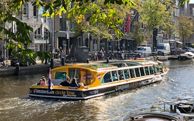 Canal cruise boat on Amsterdam canal with passengers and city buildings in the background.