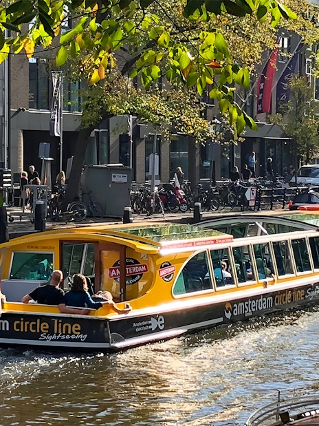 Canal cruise boat on Amsterdam canal with passengers and city buildings in the background.