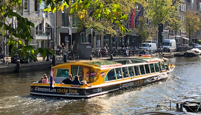 Canal cruise boat on Amsterdam canal with passengers and city buildings in the background.