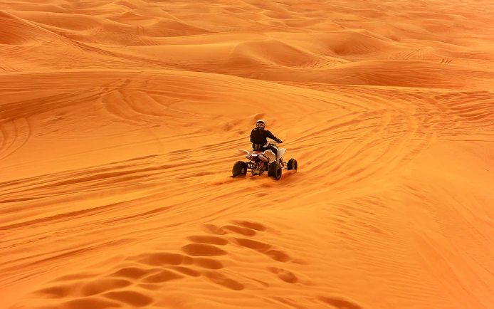Quad bike riding across desert sand dunes.