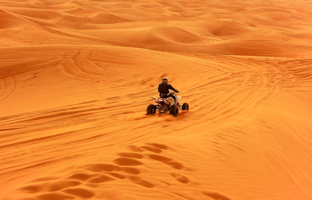 Quad bike riding across desert sand dunes.