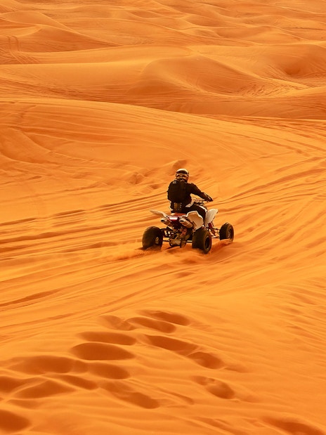 Quad bike riding across desert sand dunes.