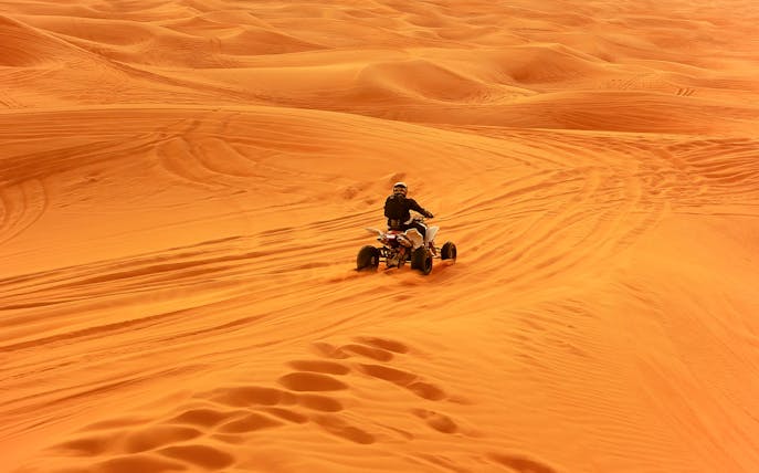 Quad bike riding across desert sand dunes.