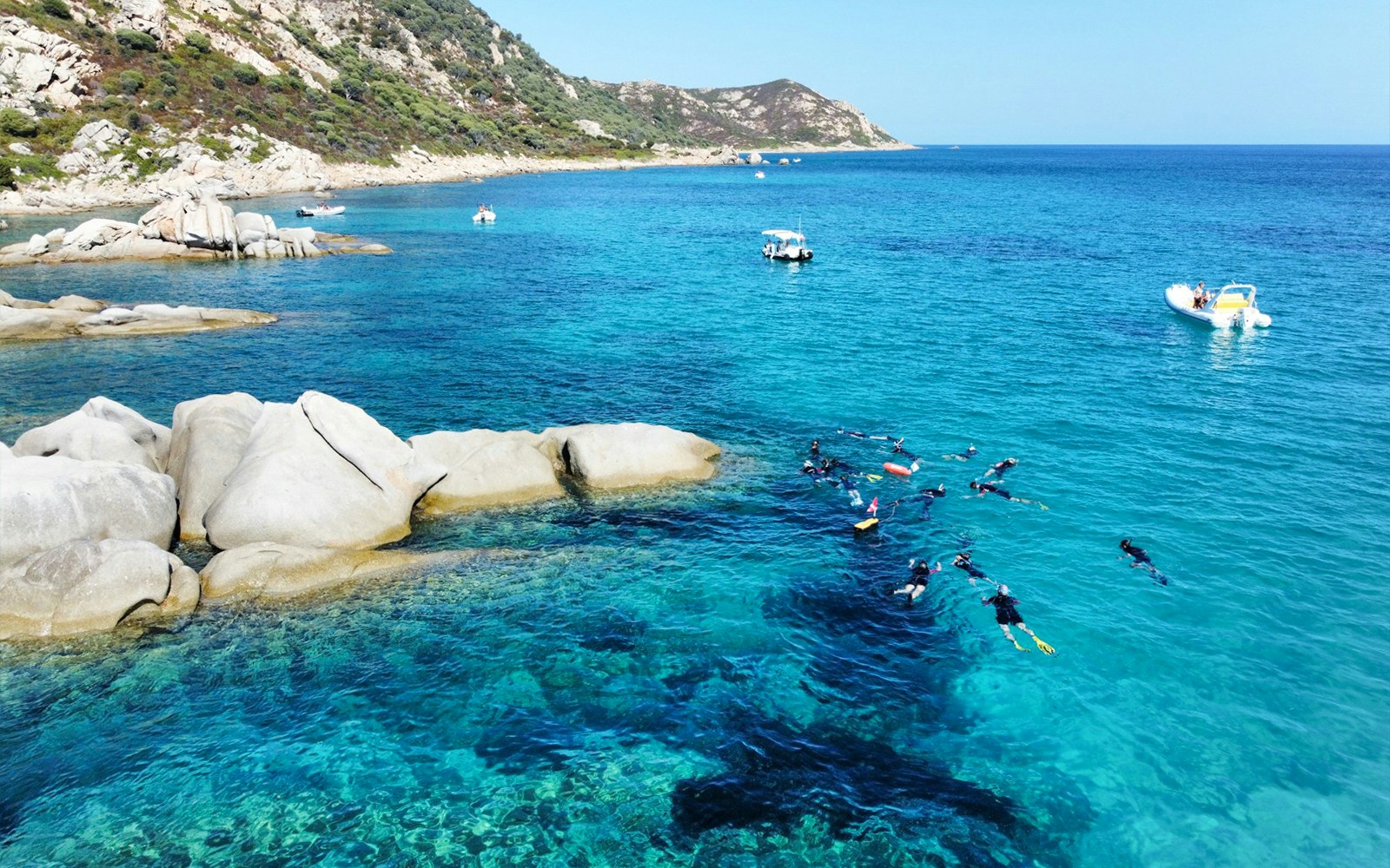 Snorkelers exploring Molara Natural Pools with boats nearby in clear blue water.
