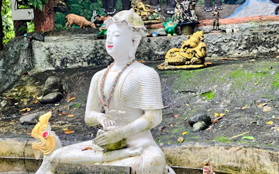 White statue of a seated figure with beaded necklaces at a temple in Chiang Mai, surrounded by small animal sculptures.