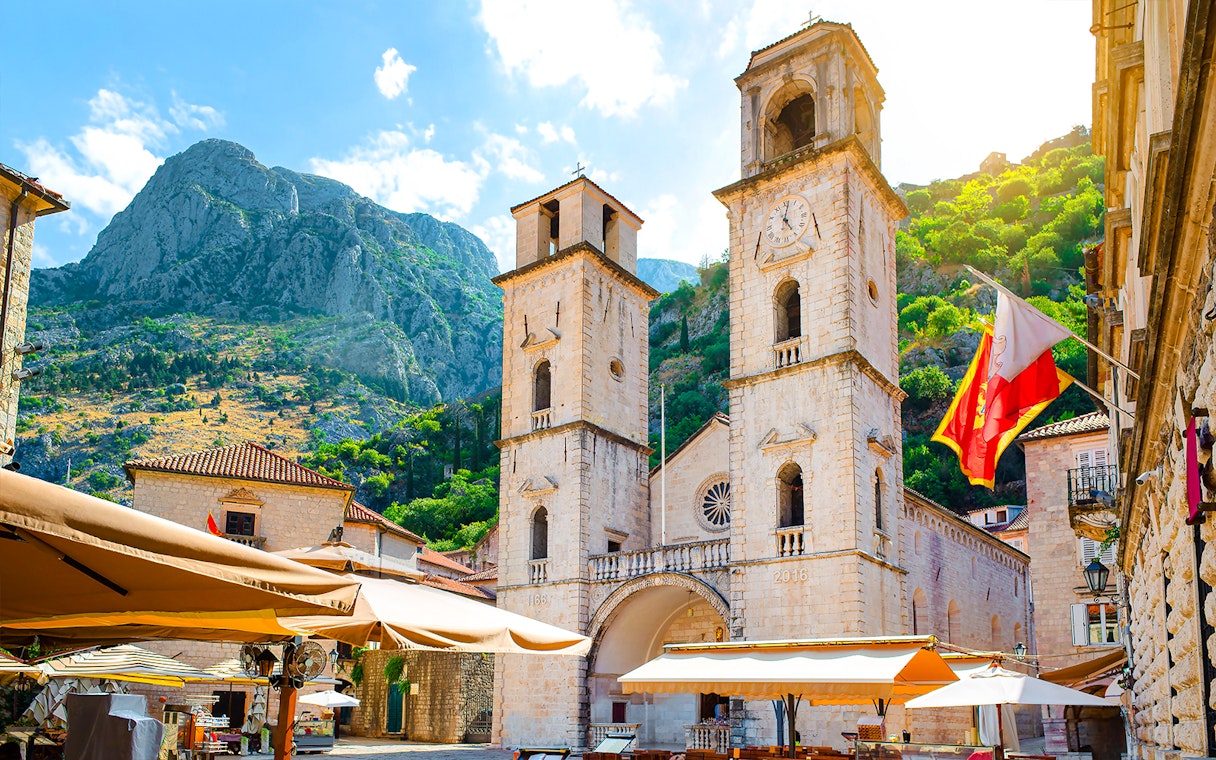 Church of Saint Tryphon with twin towers in Old Town, Kotor, against mountain backdrop.