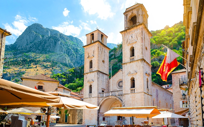 Church of Saint Tryphon with twin towers in Old Town, Kotor, against mountain backdrop.