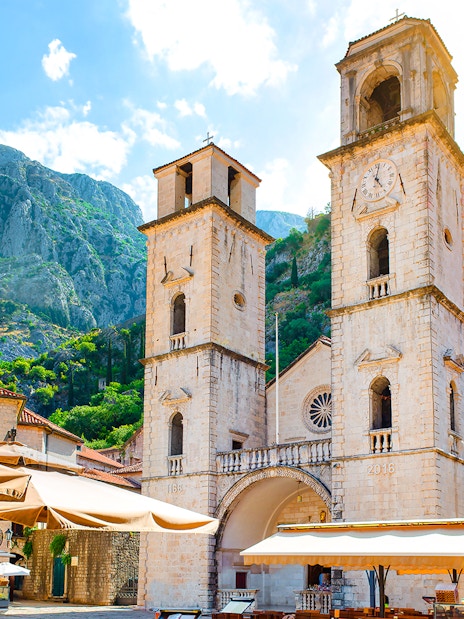 Church of Saint Tryphon with twin towers in Old Town, Kotor, against mountain backdrop.