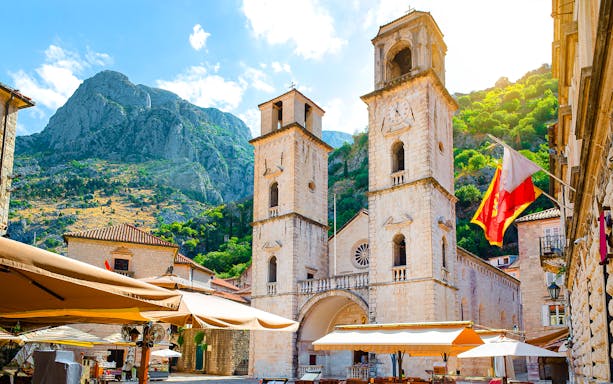 Church of Saint Tryphon with twin towers in Old Town, Kotor, against mountain backdrop.