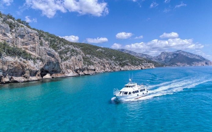 Boat cruising in the turquoise waters of Gulf of Orosei, Italy with rocky cliffs in the background.
