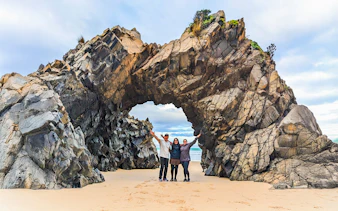 Tourists at Bruny Island exploring coastal rock arch on nature trail.