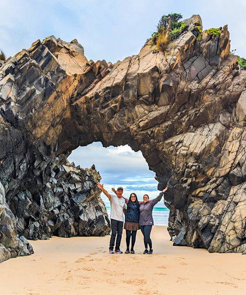 Tourists at Bruny Island exploring coastal rock arch on nature trail.