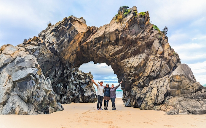 Tourists at Bruny Island exploring coastal rock arch on nature trail.