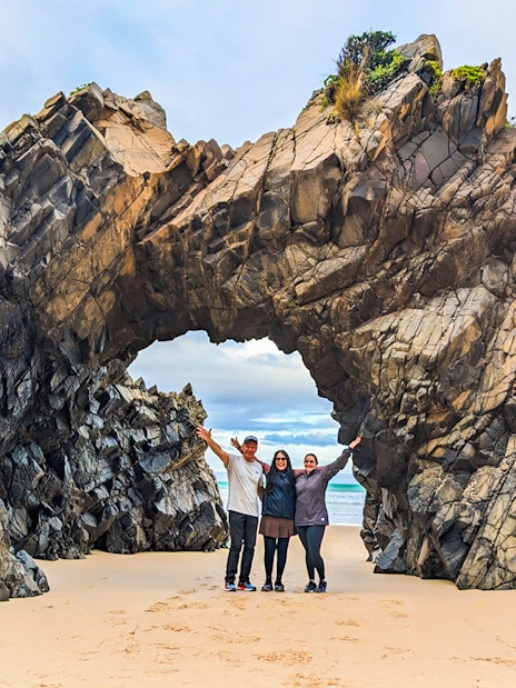 Tourists at Bruny Island exploring coastal rock arch on nature trail.