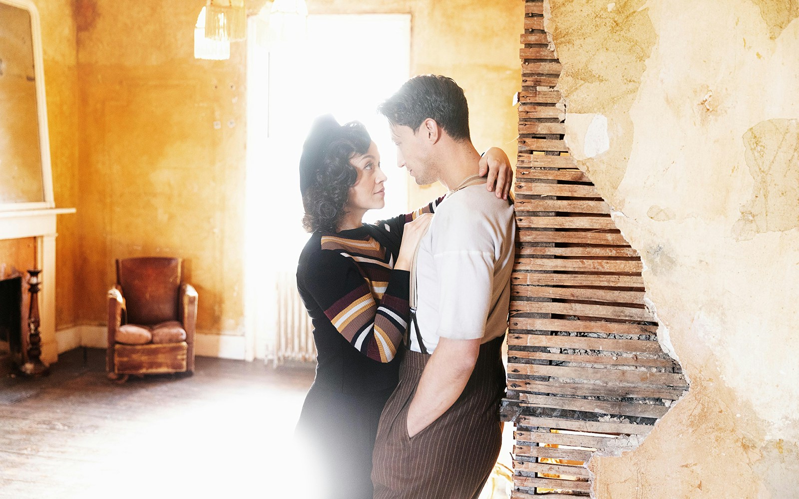Couple in vintage attire embracing in a rustic room, evoking Bonnie & Clyde era.