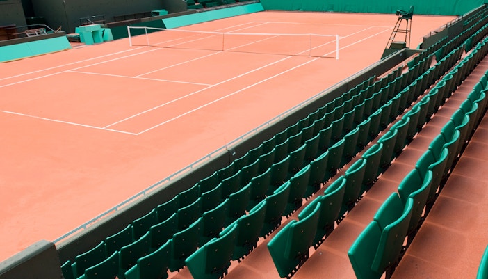 Tennis court at Stade Roland-Garros, Paris, with empty green seats and clay surface.