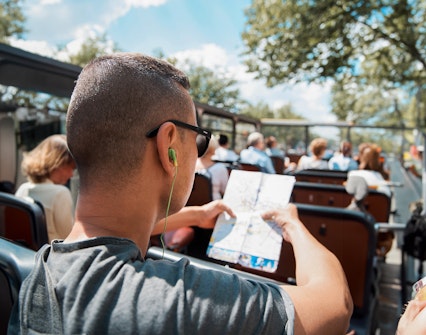 Tourist on open-top bus using audio guide and map.