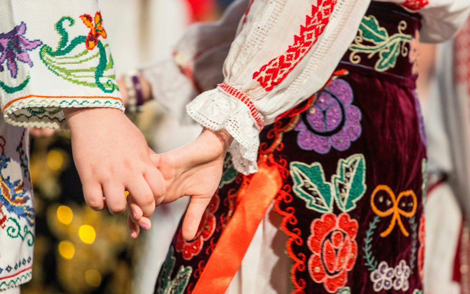 Traditional Romanian folk dancers holding hands in embroidered costumes.