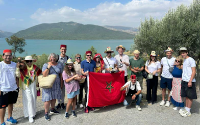 Tour group in traditional hats holding Moroccan flag by a lake in Chefchaouen, Morocco.