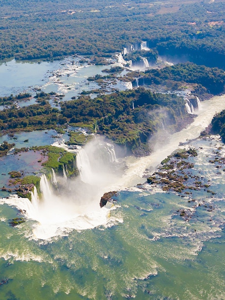Aerial view of Iguazu Falls from a helicopter ride, showcasing cascading waterfalls and lush greenery.