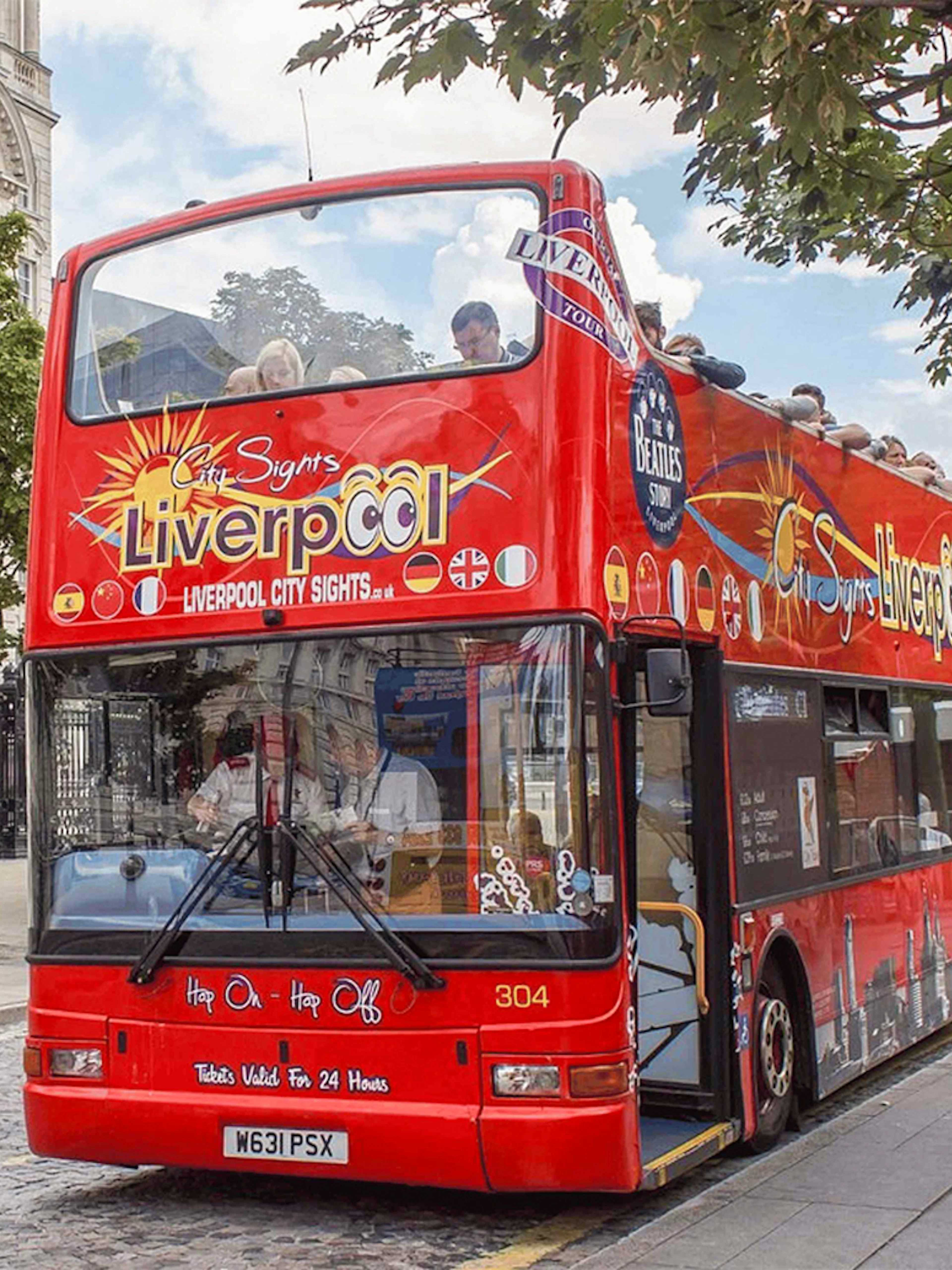 Red double-decker bus on Liverpool Hop On Hop Off City Tour near historic building.