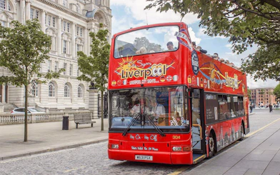 Red double-decker bus on Liverpool Hop On Hop Off City Tour near historic building.