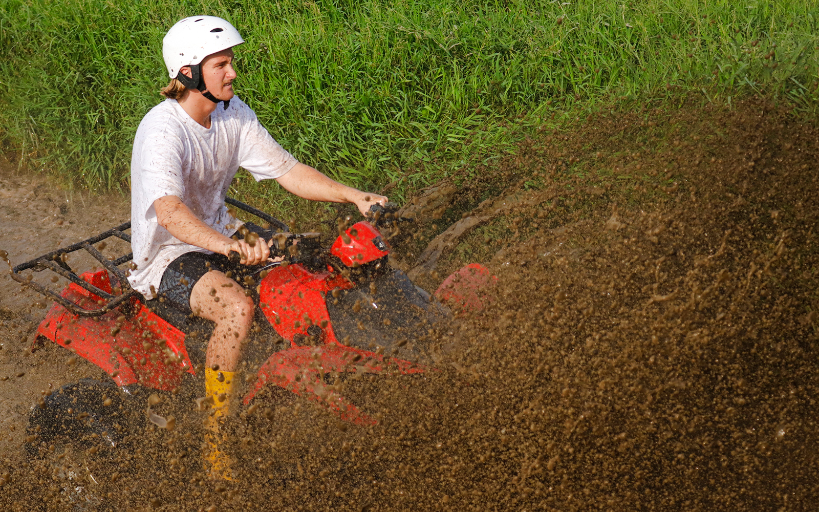 Person riding a red ATV quad bike through muddy terrain.