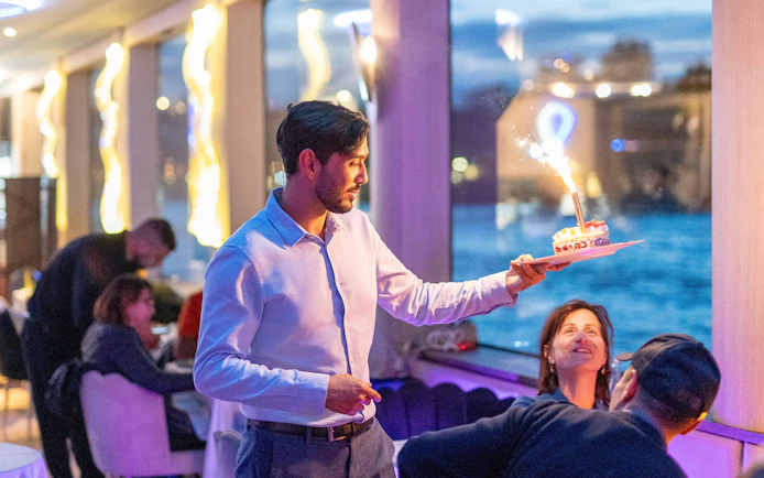Server presenting dessert with sparkler on Seine River cruise in Paris.