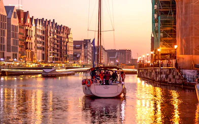 Sunset cruise boat on Gdansk River with historic buildings in the background.