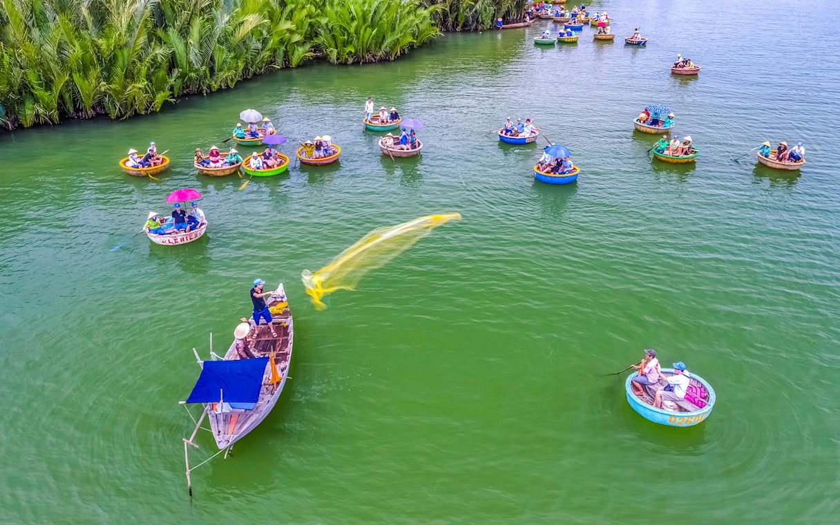 Aerial view of Hoi An fishing net activity with round boats on green water.